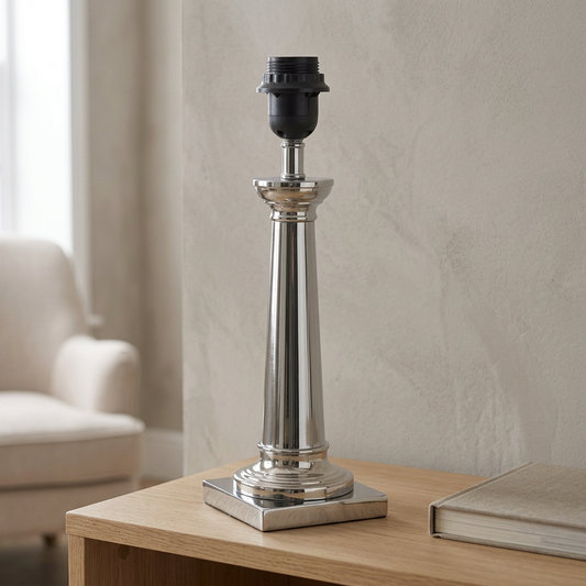 Verchromter FUKRUM-Leuchtenfuß mit konischer Säule, quadratischem Sockel und leerer schwarzer E27-Fassung auf einer hellen Holzkonsole, ohne Schirm und Leuchtmittel.