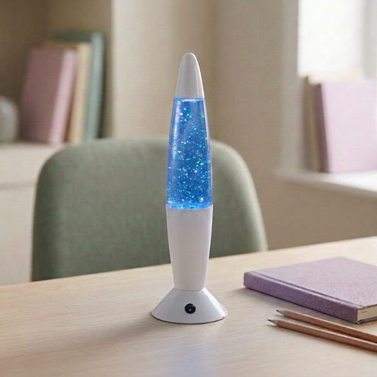 LED-Tischleuchte GLITTER mit weißem Fuß, transparentem blauem Leuchtkörper und feinen blau-grünen Glitzerreflexen auf einem hellen Schreibtisch neben einem fliederfarbenen Notizbuch