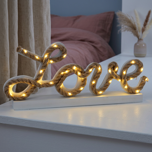 Eingeschaltete LED-Dekoleuchte LOVE aus Naturseil auf einer weißen Fensterbank im Boho-Schlafzimmer